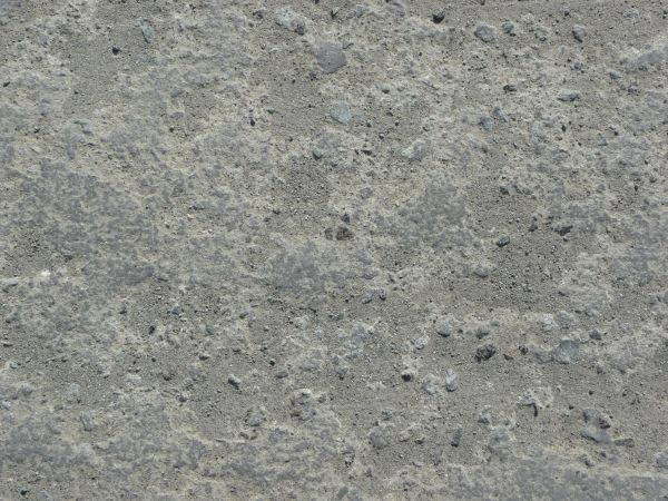 Concrete ground texture in grey tones with small rocks and rough, uneven consistency.